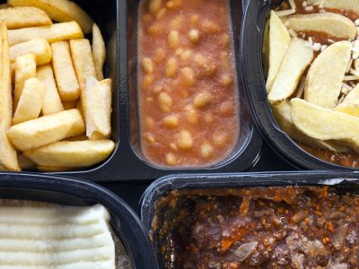 Selection of frozen, processed, ready made foods, consisting of potato chips, mince, lasagna in black, plastic containers . Microwave meals ready to heat up .