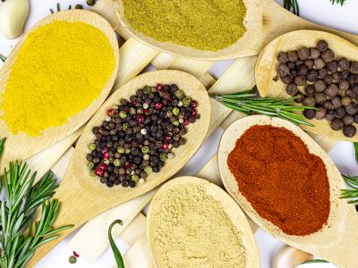 Top view of variety of spices and seasonings (indian curry, different pepper, paprika powder, salt, dry ginger and curcuma) for cooking in wooden spoons on white kitchen table background